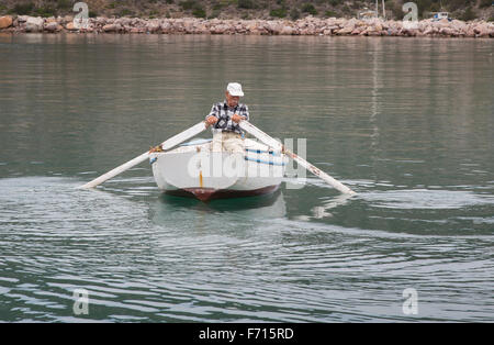 Greek fisherman rowing his boat out of the harbor at Ermioni, Greece and  into the Aegean Sea Stock Photo