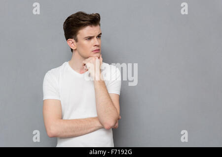 Portrait of pensive serious concentrated smug young man in white t-shirt posing on gray background Stock Photo