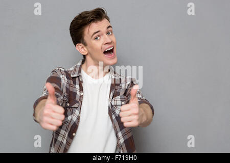 Joyful cheerful handsome pleased happy young man in plaid shirt giving thumbs up Stock Photo