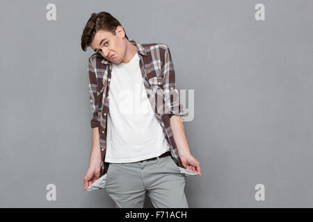 Portrait of a young man exhibiting his empty pockets on gray bakground Stock Photo