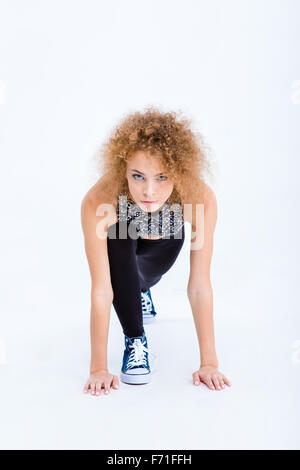 Portrait of a sports woman with curly hair standing in start position for running isolated on a white background Stock Photo