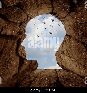 Imagination and discovery concept as a rocky cliff with an opening on top shaped as a human head as a new life metaphor and success motivation symbol with a group of birds flying high in the sky. Stock Photo