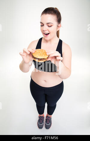Full length portrait of a fat woman eating burger isolated on a white background Stock Photo