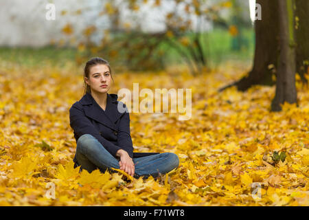 Young girl sitting on fallen leaves in autumn Park. Stock Photo