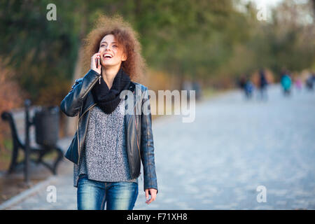Portrait of a laughing woman walking and talking on the phone outdoors Stock Photo