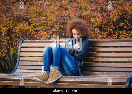 Portrait of a young sad woman sitting on the bench in autumn park Stock Photo