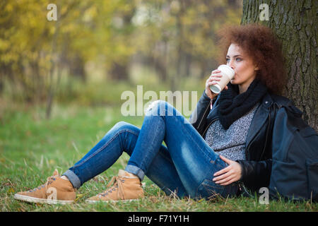 Portrait of a young beautiful woman drinking coffee under tree outdoors Stock Photo