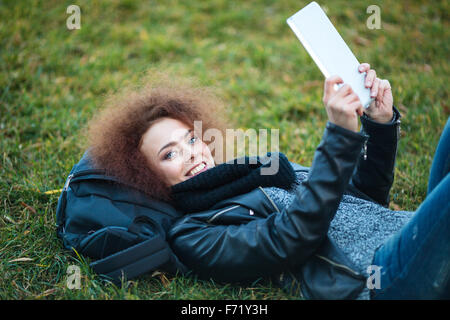 Portrait of a smiling woman lying on grass with tablet computer outdoors Stock Photo