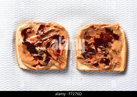 Overhead view of two slices of toasted bread with peanut butter and grape jelly. Horizontal format on a paper towel. Stock Photo
