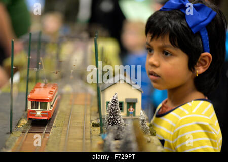 Bethpage, New York, USA. 22nd November 2015. Visitors watch as a colorful orange and beige O-Gauge trolloy passes through a winter scene. The Long Island Traction Society trolley trains layout is one of several operating layouts at the 6th Annual Nassau County Model Train Show, held at the Bethpage Senior Community Center. Stock Photo