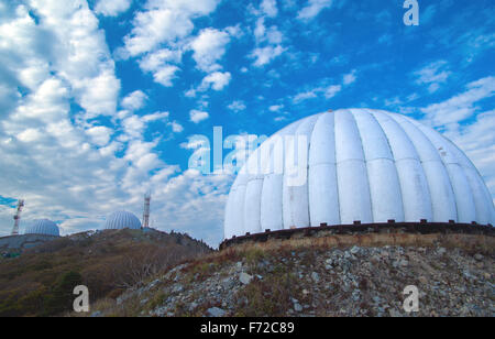 Three satellite dishes over on top of a mountain covered with protective domes on a background of clouds Stock Photo