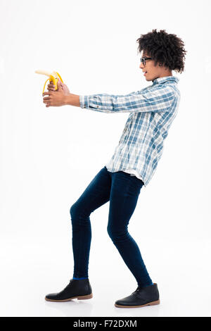 Side view portrait of a funny afro american man aiming from banana isolated on a white background Stock Photo