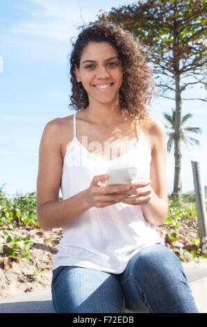 Beautiful latin woman typing message at phone and looking at camera Stock Photo