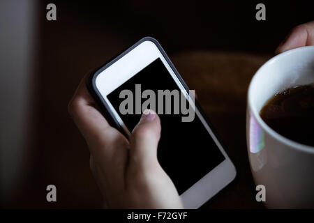 Womans hands using smartphone and holding mug Stock Photo