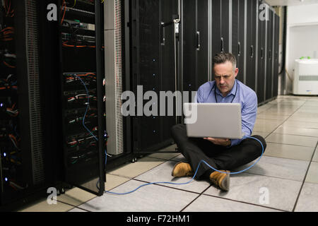 Technician using laptop to analyse server Stock Photo