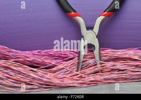 Pliers and cables on grey metal surface with violet background Stock Photo