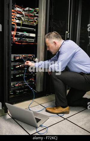 Technician using laptop to analyse server Stock Photo