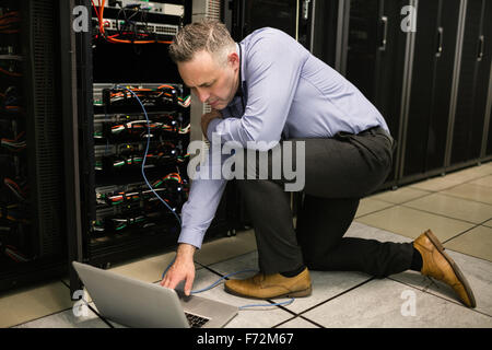 Technician using laptop to analyse server Stock Photo