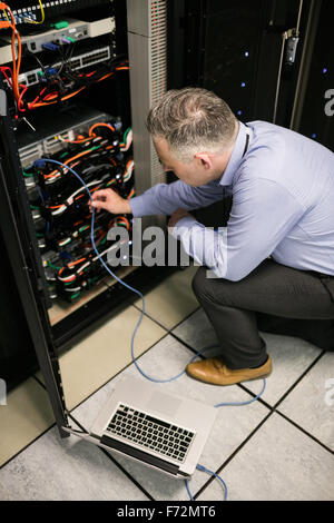 Technician using laptop to analyse server Stock Photo