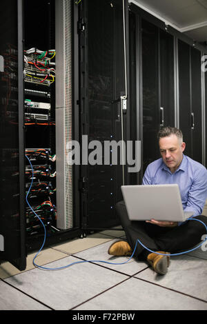 Technician using laptop to analyse server Stock Photo