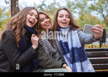 Portrait of a three cheerful girlfriends making selfie photo on smartphone outdoors Stock Photo