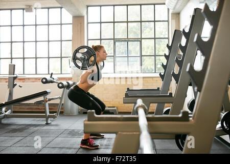 Focused young woman lifting weights in health club. Fitness female doing squats in gym. Stock Photo