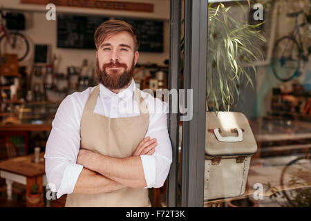 Portrait of a handsome and confident cafe owner standing at the door. Young man standing with his arms crossed looking at camera Stock Photo