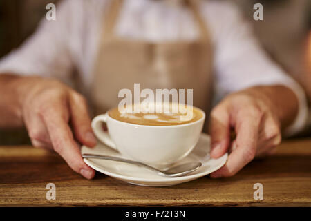 Close up of man serving coffee while standing in coffee shop. Focus on male hands placing a cup of coffee on counter. Stock Photo