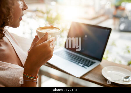 Cropped image of woman drinking coffee with a laptop on table at a restaurant. Young girl holding a cup of coffee at cafe. Stock Photo