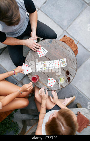 Three young friends playing cards at cafe. Directly above shot of young man and women sitting around an outdoors cafe table and Stock Photo