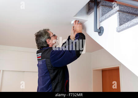 Caretaker in a staircase mounted and checks a smoke detector Stock Photo