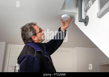 Caretaker in a staircase mounted and checks a smoke detector Stock Photo