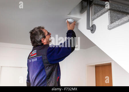 Caretaker in a staircase mounted and checks a smoke detector Stock Photo