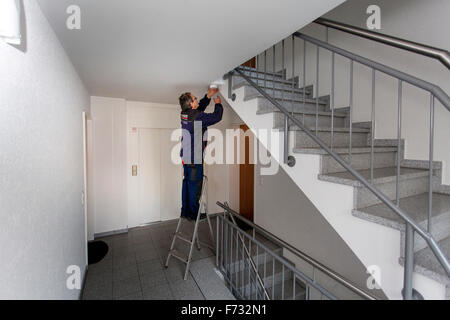Caretaker in a staircase mounted and checks a smoke detector Stock Photo