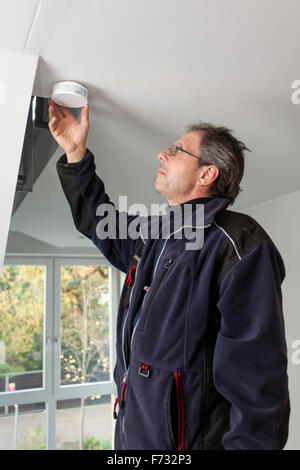 Caretaker in a staircase mounted and checks a smoke detector Stock Photo