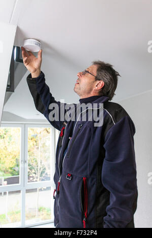 Caretaker in a staircase mounted and checks a smoke detector Stock Photo