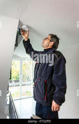 Caretaker in a staircase mounted and checks a smoke detector Stock Photo