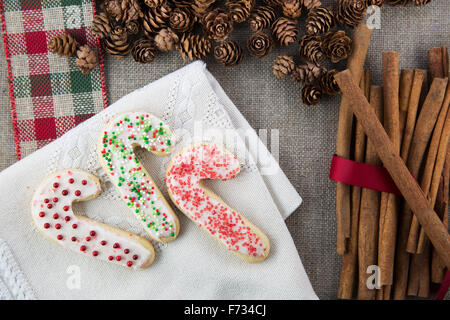 Three frosted and decorated candy cane shaped sugar cookies on a cloth napkin with cinnamon sticks and pine cones Stock Photo