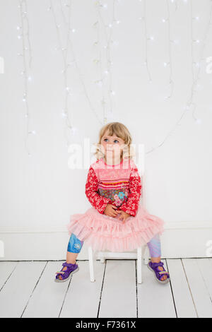 Young girl sitting on a chair in a photographers studio, posing for a picture. Stock Photo