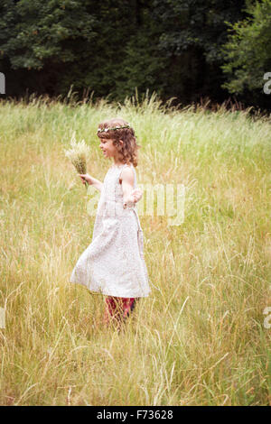Young girl with flowers in her hair picking wild flowers in a meadow. Stock Photo