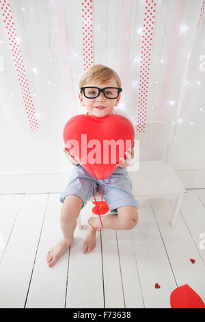 Young boy posing for a picture in a photographers studio, holding red balloons. Stock Photo