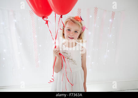 Young girl posing for a picture in a photographers studio, holding red balloons. Stock Photo