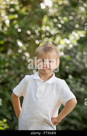 Young boy standing in a forest, looking at the camera, pulling a face. Stock Photo