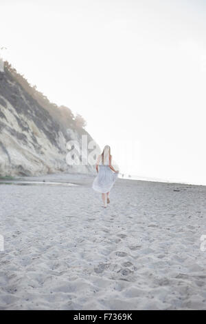 Blond woman walking on a sandy beach near a cliff. Stock Photo