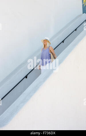 Blond woman wearing a hat walking down a staircase. Stock Photo