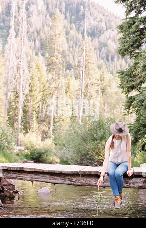 Woman sitting on a wooden bridge over a stream. Stock Photo