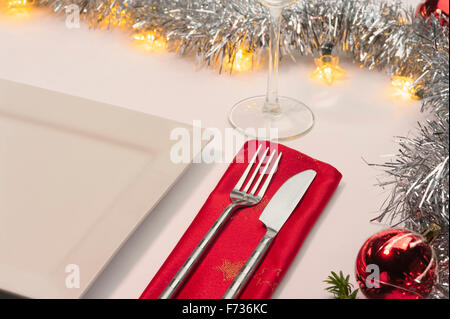 Table laid for Christmas dinner, decorated with baubles and tinsel and fairy lights. Knife fork and red napkin. Stock Photo