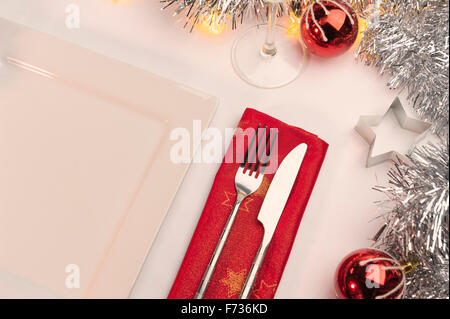 Table laid for Christmas dinner, decorated with baubles and tinsel and fairy lights. Knife fork and red napkin. Stock Photo