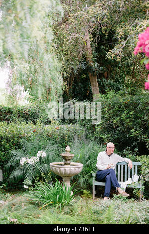 Man sitting on a wooden bench in a garden, taking a break. Stock Photo