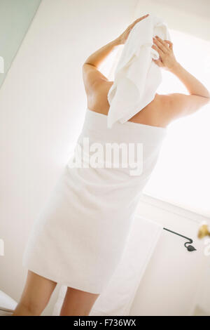 Woman wrapped in a white towel standing in a bathroom, wrapping her hair in a towel. Stock Photo